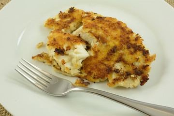 Cooked spicy chipotle breaded tilapia fish fillet on white plate with fork