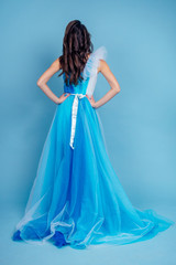 Fototapeta premium Young beauty woman in tulle fluttering blue dress.Beautiful girl with make-up , hairstyle and gorgeous look.female model prom seamstress and designer clothes tailor on a blue background in the studio