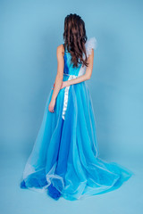 Young beauty woman in tulle fluttering blue dress.Beautiful girl with make-up , hairstyle and gorgeous look.female model prom seamstress and designer clothes tailor on a blue background in the studio