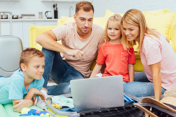 happy family using laptop, planning summer vacation, packing luggage and having great time, travel concept