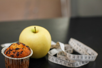 Close up delicious yellow apple with cupcake and measuring tape on black wooden table.