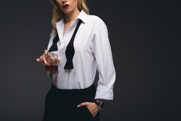 cropped view of elegant girl in formal wear holding glass of whiskey, isolated on dark grey