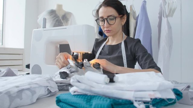 Hobby sewing and a small business concept. Young pretty woman seamstress sews on sewing machine. Tailor making a garment in her workplace