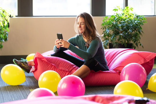 Woman Sitting On Pink Bean Bag Chair Looking At Phone