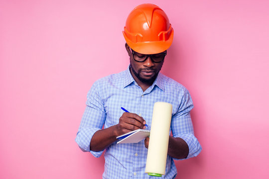 Black Man African American Holding Paint Roller In Hand Paints The Wall In Pink Color .happy African Builder Painting Inside The House,businessman Wears A Helmet Hard Hat.young Guy Is Painting