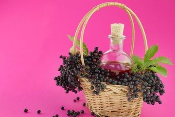 Obraz na płótnie Canvas Elderberry syrup.Tincture of elderberry berries in a glass bottle, black elderberry berries in a wicker basket on a bright fuchsia background.Alternative useful syrups