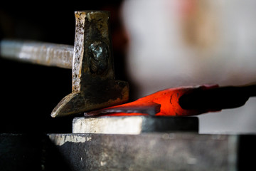 Blacksmith working with red hot metal of new axe on the anvil at the forge Macro photo