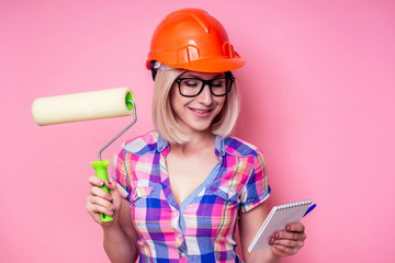 Female painter hold shopping list and roller for refurbishing color of pink wall indoors.smiling...