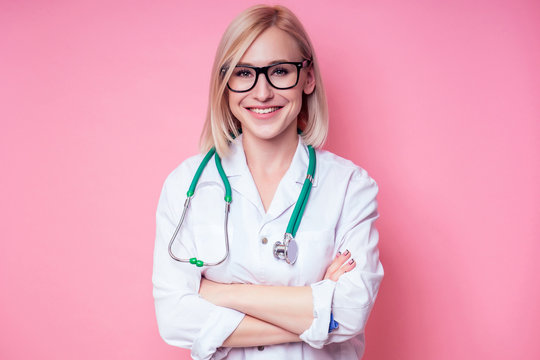 Portrait of a smiling female gynecologist doctor.beautiful blonde woman in white medical coat and glasses holding a stethoscope on a pink background in the studio.beautician perfect skin