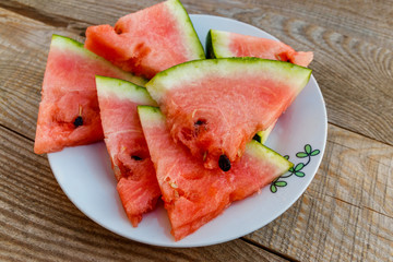 Fresh ripe sliced watermelon in white plate on rustic wooden table