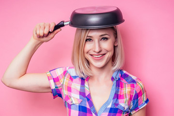 Beautiful blonde housewife woman holding pan on a pink background in the studio