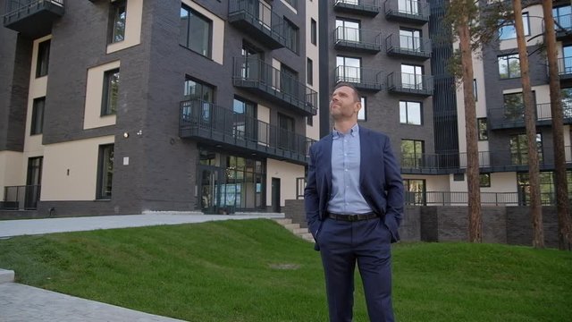 Adult ambitious manager portrait in elegant formal casual wearing. Real property development. Leader man standing on the garden of residental area, enjoy the scenery summer nature and resting