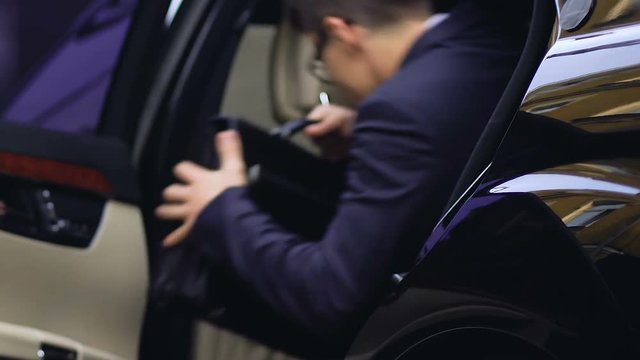 Rich businessman getting into car, personal driver closing door of auto, vip