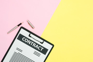 Flat lay design of office desk working space  - Top view of a contract document and a pen on pink and yellow pastel color with copy space. Pastel color screen working space background.