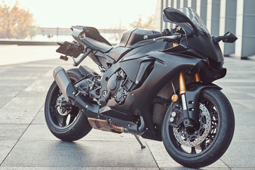 Close-up photo of a black superbike outside near building. - Powered by Adobe