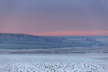 Beautiful winter sunset. The first snow in the fields at sunset.