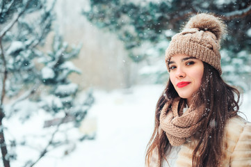 close up winter portrait of smiling young woman walking in snowy forest with trees on background