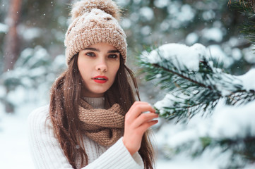 close up winter portrait of dreamy young woman walking in snowy forest with trees on background