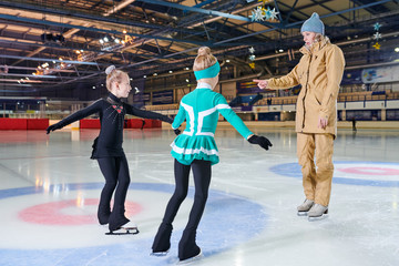 Full  length portrait of woman coach  training  two little girls figure skating in indoor rink