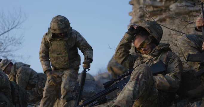 Medium slow motion shot of soldiers taking a rest during an assault and removing their helmets
