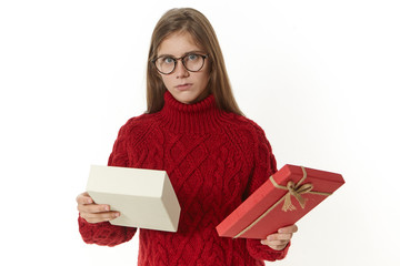 Horizontal shot of displeased or confused young woman wearing spectacles and knitted sweater posing...