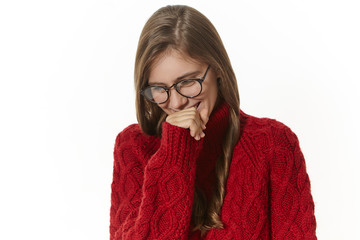 Portrait of attractive joyful girl with loose hair holding hand at her mouth, laughing at joke or...
