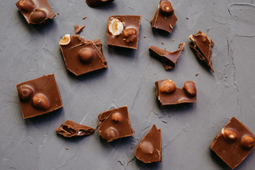 Top view Broken chocolate pieces with hazelnuts on gray background