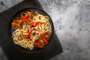Traditional Asian food - noodles with seafood, salad, red pepper and fried mushrooms are on a gray table. Copy space. Top view