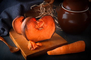 Honey baked pumpkin on a wooden board next to carrots on a background of a rural ceramic pot