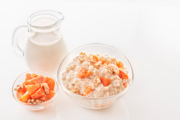 Oatmeal with pumpkin and nuts in a glass plate and a jug with milk on a white background. Close-up. Copy space