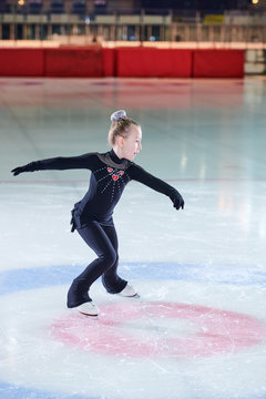 Full length portrait of little girl figure skating beautifully during competition or training in indoor rink, copy space