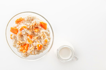 Fototapeta na wymiar Oatmeal with pumpkin and nuts in a glass plate and a jug with milk on a white background. Copy space. Top view