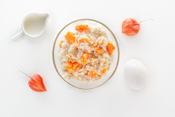 Fototapeta na wymiar Oatmeal with pumpkin and nuts, egg and a jug of milk on a white background. View from above.