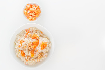 Fototapeta na wymiar Oatmeal with pumpkin and nuts in a white plate on a white background. View from above. Copy space.