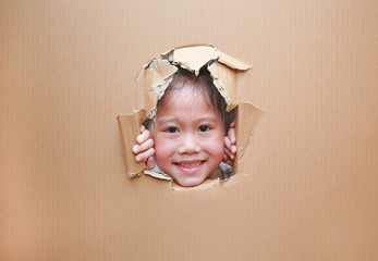 Happy Asian kid girl looking through hole on cardboard with copy space.