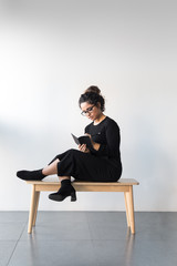 Beautiful woman with curly hair dressed on black wearing glasses and writing on a notebook with a black pencil