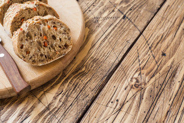 Fresh bread with sunflower seeds, sesame seeds and flax are cut into pieces on a cutting board. Wooden background, copy space
