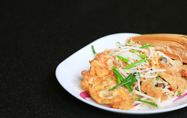 Fried mussel pancakes in white plate on black table, Thai food.