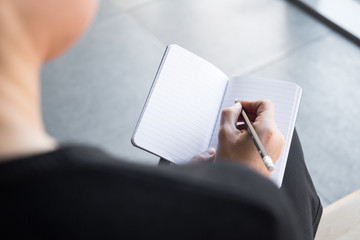 Beautiful woman with curly hair dressed on black wearing glasses and writing on a notebook with a black pencil