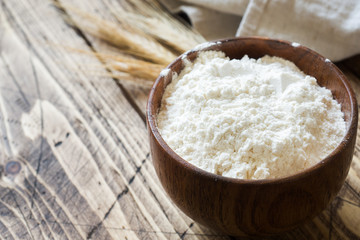 Flour in wooden bowl and wheat ears on wooden background. Copy space.