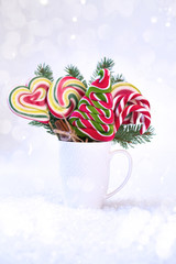 Christmas or new year card. Cup with fir tree branch and colored lollipops in the shape of the Christmas tree on the snow background. Copy space