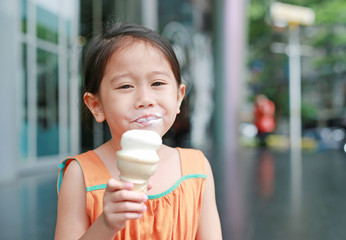 Happy little Asian kid girl enjoy eating ice cream cone with stained around her mouth.