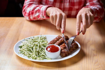 Woman cuts sausage grill with a fork and knife in a restaurant, in a red plaid shirt. selective focus.restaurant. copy space for design menu