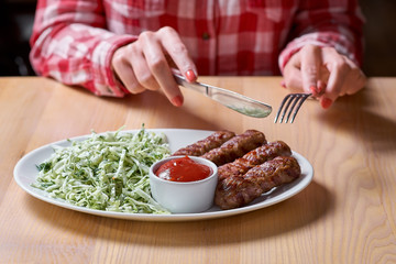 Woman cuts sausage grill with a fork and knife in a restaurant, in a red plaid shirt. selective focus.restaurant. copy space for design menu