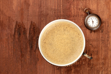 A cup of coffee and an old pocket watch showing 7 o'clock, shot from above on a dark rustic wooden background with copy space