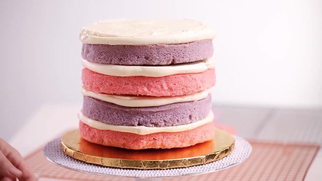 Baker assembling pink and purple cake layer to make unicorn cake for little girl's birthday party.