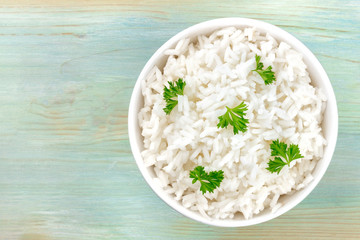 An overhead photo of a bowl of cooked white long grain rice, shot from above on a teal blue background with a place for text