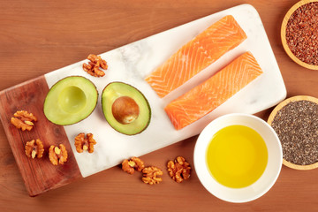 Fototapeta na wymiar Healthy omega 3 diet food products. Raw salmon, avocado, walnuts, chia seeds, and flax seeds, shot from above on a dark rustic wooden background with copy space