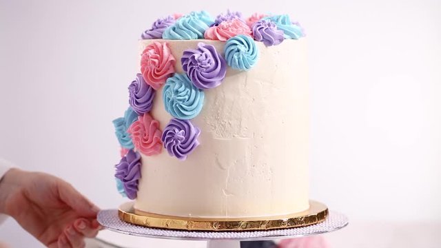 Baker piping pastel color buttercream rosettes on a white cake to make a unicorn cake.