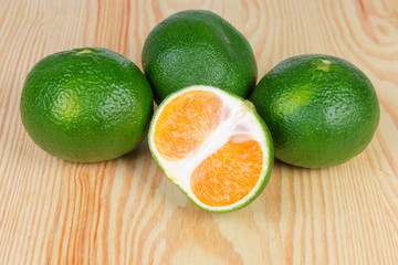 Half and several whole ripe green tangerines on wooden surface